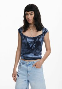 Navy blue, fitted tank top with a scoop neckline and cap sleeves, displayed with light blue denim shorts featuring floral embroidery.