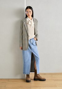 Blazer à carreaux, pull en crème à côtes, cravate blanche, jupe en jean bleu avec fente latérale et bottes à lacets marron avec semelles épaisses.