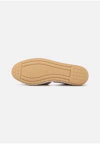 Shoe sole with textured rubber material, featuring a series of circular and rectangular patterns for traction, and a light brown color.