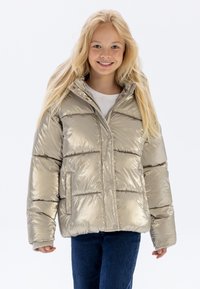Gul puffjacka med en glänsande yta, horisontellt kviltat mönster, framfickor och hög krage, bärs över en vit skjorta och jeans.