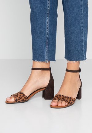 Fødder iført leopardmønstret åbne sandaler med blokhæl og ankelremme, kombineret med cropped blå cowboybukser med frynsede kanter.