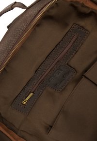 Brązowe skórzane wnętrze torby z zamykaną na zamek kieszenią, naszywką z napisem "Venezia" oraz elegancką, gładką teksturą.