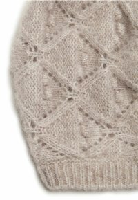Ljusbeige stickad textil med ett diamantspetsmönster, fluffig textur och ribbad nederkant. Naturliga fibrer skapar ett mjukt utseende.