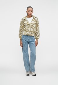 Pullover bege fofinho com padrão floral e fecho em zip, combinado com jeans de perna reta azul claro e sapatilhas brancas.