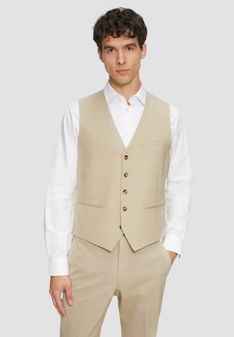 Beige Weste aus einem strukturierten Stoff, mit einem V-Ausschnitt, fünf braunen Knöpfen und zwei Taschen, kombiniert mit einem weißen Hemd.