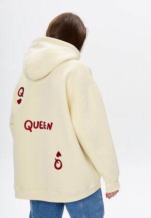 Geel oversized hoodie met rode geborduurde tekst "QUEEN" en een speelkaartsymbool, zachte textuur en een kangoeroezak.