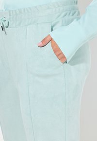 Light blue, soft suede joggers with an elastic waistband, featuring a pocket on the side and a smooth texture.