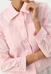 Lys pink denimjakke med krave, knaplukning foran og to brystlommer. Har matchende knapper og en afslappet pasform med opkrøllede ærmer.