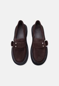 Ζευγάρι από σκούρα καφέ μοκασίνια από καστόρι χωρίς κορδόνια με μαύρες σόλες και λεπτομέρεια ασημένιας πόρπης, με την επωνυμία "Zign Studio" στο εσωτερικό.