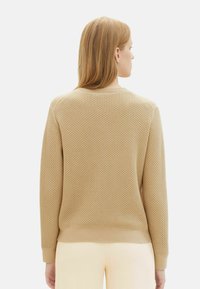 Felpa beige a maglia con un motivo a nido d'ape testurizzato, polsini a costine e scollatura rotonda, con un orlo aderente in vita.