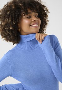 Pull en col roulé bleu clair avec un col et des poignets côtelés, fabriqué en tissu doux et texturé, avec des manches ajustées et un design décontracté.
