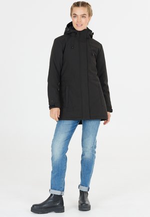 Schwarze wasserfeste Jacke mit Kapuze, Reißverschluss und Kordelzügen. Ein Paar hellblaue Jeans und schwarze Knöchelstiefel. Einfaches, funktionales Design.