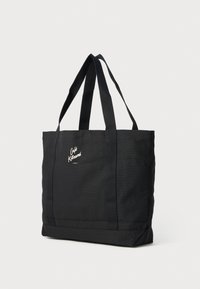 Svart tøy tote bag med to sterke håndtak, med en teksturert overflate og en hvit logo på fronten. Rektangulær form, minimalistisk design.