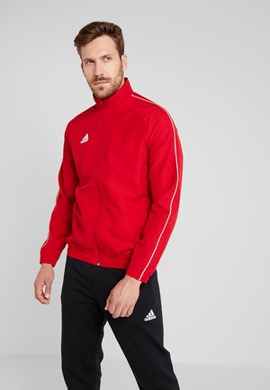 Red zip-up track jacket with white side stripes, featuring a high collar and elastic waistband. Paired with black pants.