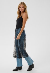 Schwarzes Spitzentop mit Spaghettiträgern über hellblauen ausgestellten Jeans, kombiniert mit schwarzen Stiefeln mit Absatz und einem goldenen Armreif.