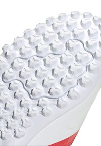 Suela de zapato de fútbol con goma blanca texturizada, presenta tacos hexagonales para tracción y un acento rojo en el talón.