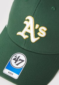 Zelená baseballová čiapka s vyšitým bielym a žltým logom "A's". Obsahuje štítok s nápisom "47 KIDS" a textúrovanú tkaninu.