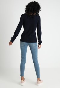 Marineblauwe ribgebreide trui, ronde hals, aangesloten mouwen; gedragen met lichtblauwe skinny jeans en lichtroze sneakers; zachte texturen.