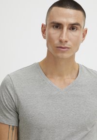 Siva v-neck majica iz mehkega, lahkega materiala. Ima gladko teksturo in čiste šive okoli ovratnika.