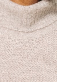 Lichtbeige gebreide trui met een hoge, geribbelde col. Zachte textuur met een losse, ademende steek en subtiele details.