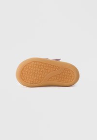Suela de goma con un patrón texturizado, de color marrón claro. La parte superior está hecha de un material de ante rosado con una correa de gancho y bucle.