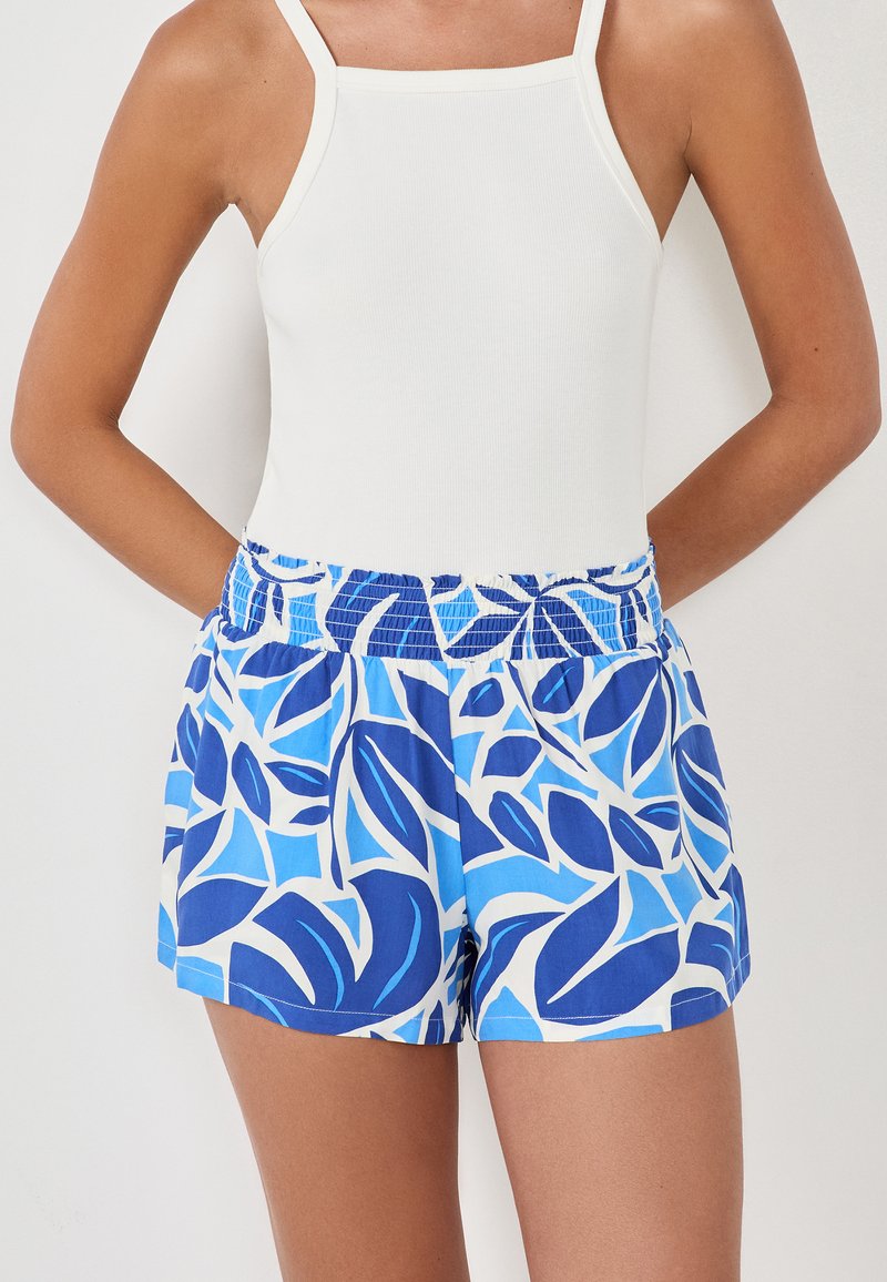 Blauwe bloemen zwembroek met een elastische tailleband en witte accenten, met een tropisch loof patroon op een lichtblauwe achtergrond.