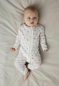 Baby-Overall aus weichem weißen Stoff mit einem Reißverschluss, der mit kleinen braunen Tiermotiven und Spitzenakzenten an den Bündchen verziert ist. Glatte Textur.