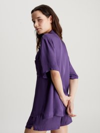 Cămașă scurtă din satin mov, cu un croi lejer, având o buzunar pe piept și fante laterale, asortată cu pantaloni scurți corespunzători.