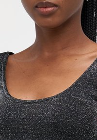 Svart, glitrende topp med rund hals. Stoffet har en glitrende tekstur med en tettsittende passform som fremhever kragebeinet.