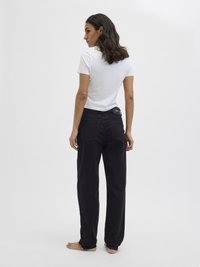 Λευκό κοντομάνικο μπλουζάκι συνδυασμένο με μαύρο παντελόνι φάρδους που έχει πίσω τσέπες και εμφανή ετικέτα λογότυπου στη ζώνη.