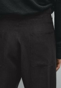 Tummat pellavahousut, joissa on kaksi takataskua, sileä pintatekstuuri ja suora leikkaus, näkyvissä vyötäröstä alaspäin.