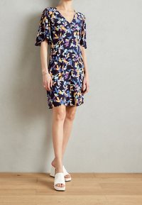 Klänning med blommönster och djup V-ringning, korta luftiga ärmar och avslappnad passform, tillsammans med vita blockklacken sandaler.