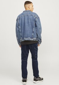 Chaqueta de mezclilla en azul claro con un corte relajado, que presenta un cierre de botones y costuras visibles, combinada con pantalones cargo azul oscuro y zapatillas.