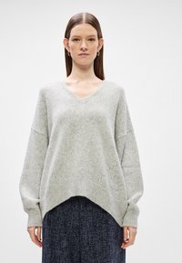 Sweater oversized cinza claro com decote em V, punhos e bainha canelados. Textura suave e ombros caídos complementam um ajuste descontraído.