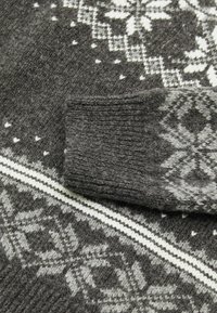 Maglione grigio con un lavorazione a maglia strutturata, caratterizzato da un motivo a fiocchi di neve bianco e grigio chiaro. Il polsino presenta dettagli a coste e una striscia a contrasto.