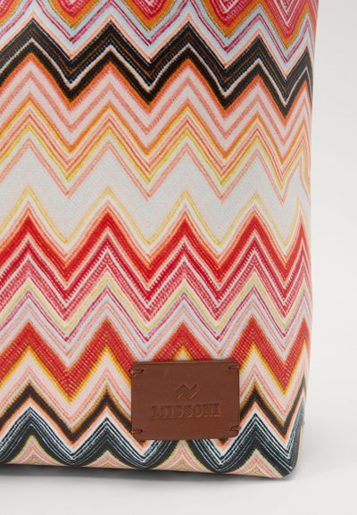 Geantă cu un model zigzag multicolor în nuanțe de roz, roșu, portocaliu, negru și alb. Prezintă o etichetă din piele maro cu text embosat.