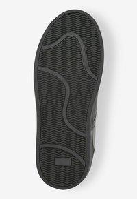 Svart gummisula med en vågig mönstring och präglade detaljer, designad för grepp och hållbarhet. Släta kantkanter.