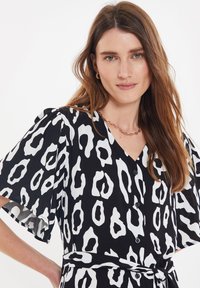 Vestido en blanco y negro con un corte suelto, escote en V, mangas cortas tipo volantes, botones y un patrón abstracto de leopardo.