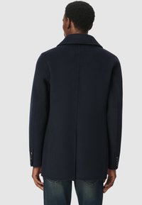 Granatowy płaszcz z mieszanki wełny z klasycznym kołnierzem, prostym krojem i zapięciem na guziki przy mankietach. Gładka tekstura i czyste linie w widoku z tyłu.