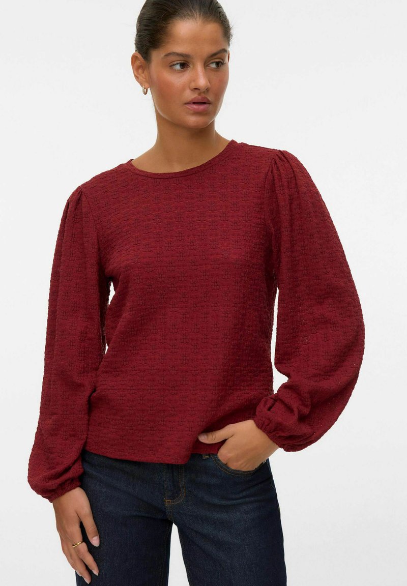 Bordeauxfärgad, texturerad långärmad topp med puffärmar och rund halsringning, kombinerad med mörka jeans. Diskret mönster i hela tyget.