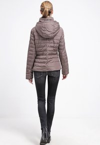 Padded brown jacket with a hood, featuring quilted design and ribbed cuffs, paired with slim black jeans and ankle boots.