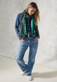 Jeansjacka i mörkblått, vit t-shirt, ljusblå jeans och svart/grön mönstrad scarf. Neutrala sneakers fulländar outfiten.