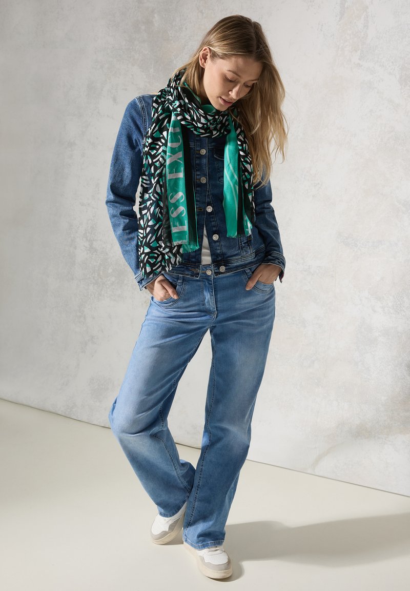 Jeansjacka i mörkblått, vit t-shirt, ljusblå jeans och svart/grön mönstrad scarf. Neutrala sneakers fulländar outfiten.