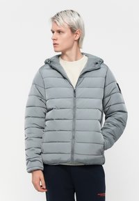 Grå polstret jakke med hætte, lynlåslukning og horisontale syninger. Letvægtsstof med en glat tekstur. Ingen synlige mønstre eller detaljer.