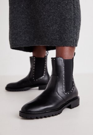 Bottes basses en cuir noir avec des clous argentés et des panneaux latéraux élastiques portées avec une jupe en laine gris foncé.