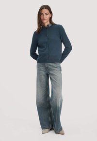 marineblauer Cardigan mit Rundhalsausschnitt, Knöpfen vorne und gerippten Bündchen, kombiniert mit hoch taillierten, weit geschnittenen hellblauen Jeans.