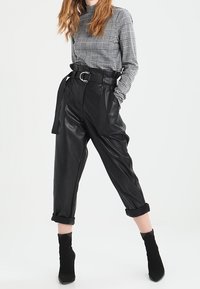 Svarta konstläderbyxor med hög midja, bälte och uppvikta fållar, kombinerat med en grå rutig långärmad topp. Slät textur.