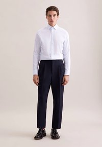 Lichtblauw overhemd met knopen, gecombineerd met donkerblauwe, op maat gemaakte broek met een gladde textuur en een slanke pasvorm, afgewerkt met zwarte schoenen.