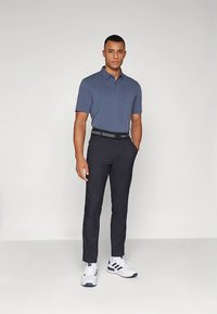 Μπλε ναυτικό πόλο πουκάμισο, μαύρο παντελόνι στενής γραμμής και λευκά αθλητικά παπούτσια με μπλε ναυτικές λεπτομέρειες. Ομαλή υφή, απλός σχεδιασμός και ελάχιστες λεπτομέρειες.