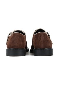 Brązowe zamszowe buty z zaokrąglonym czubkiem, czarną gumową podeszwą i gładką skórzaną lamówką. Posiadają regulację z detalem klamry z tyłu.